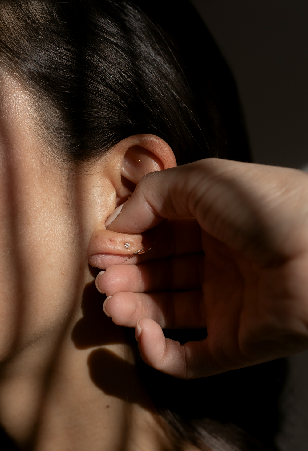 A 24K gold ear seed applied to the ear by hand in soft natural light — VIE HEALING needle-free auriculotherapy